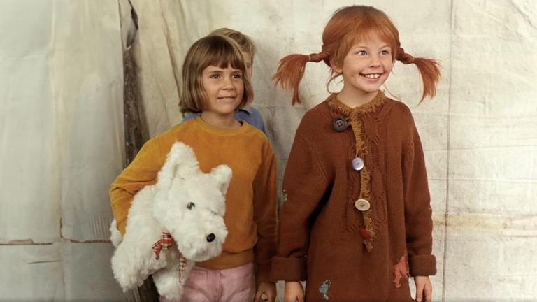 Pippi und Annika schauen begeistert einer Vorführung zu. Hinter den beiden steht Tommi ganz versteckt und Annika hat einen weißen Stoffhund unterm Arm