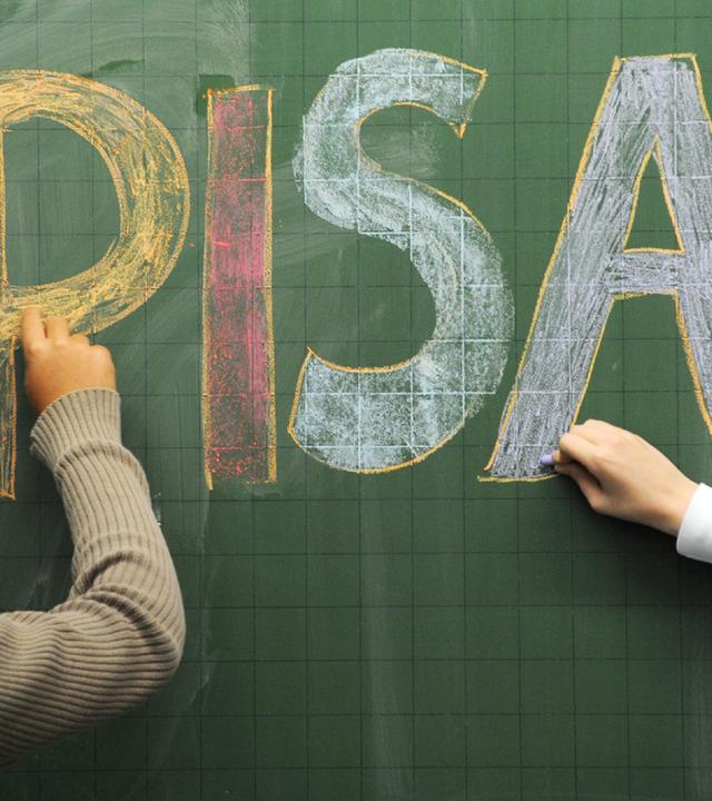 Schüler schreiben "PISA" mit farbiger Kreide an eine Tafel