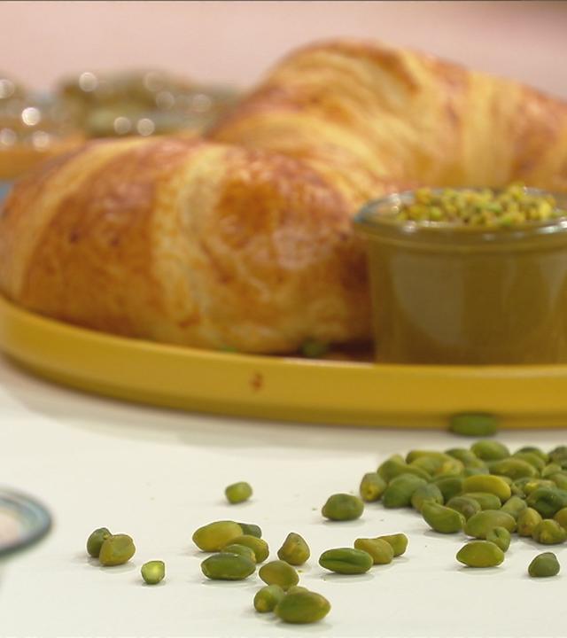 Pistazien liegen auf Tisch; Croissant im Hintergrund