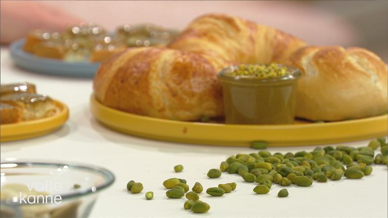 Pistazien liegen auf Tisch; Croissant im Hintergrund