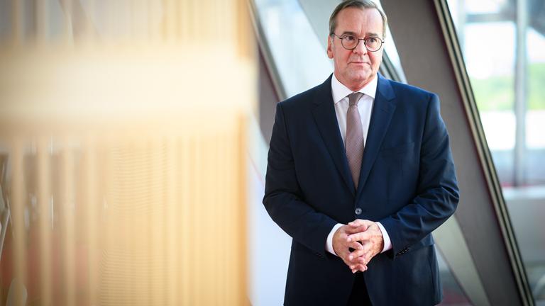 Verteidigungsminister Boris Pistorius steht vor einem Fenster und schaut an der Kamera vorbei. 