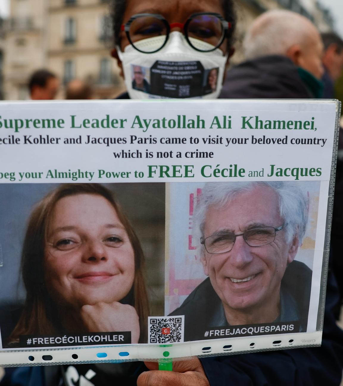 Eine Frau hält ein Plakat mit einem Bild von Cécile Kohler und Jacques Paris, die im Mai 2022 während einer Touristenreise in den Iran verhaftet wurden.