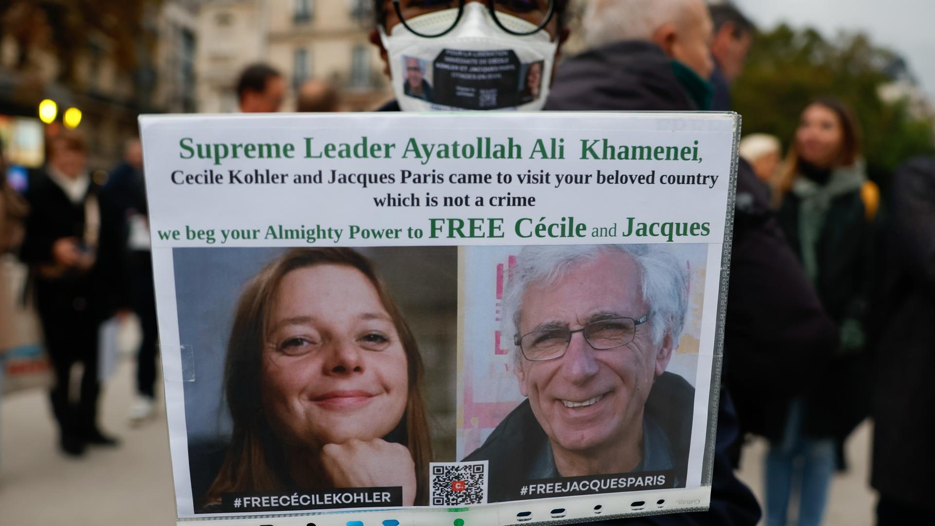 Eine Frau hält ein Plakat mit einem Bild von Cécile Kohler und Jacques Paris, die im Mai 2022 während einer Touristenreise in den Iran verhaftet wurden.