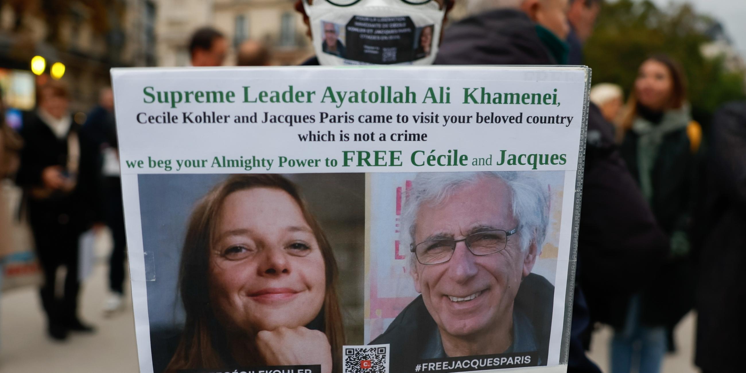 Eine Frau hält ein Plakat mit einem Bild von Cécile Kohler und Jacques Paris, die im Mai 2022 während einer Touristenreise in den Iran verhaftet wurden.