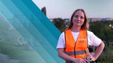Eine Frau mit blonden, schulterlangen Haaren schaut in die Kamera. Sie trägt eine Warnweste mit der Ausschrift "A-Team".