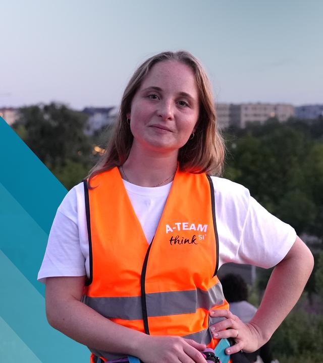 Eine Frau mit blonden, schulterlangen Haaren schaut in die Kamera. Sie trägt eine Warnweste mit der Ausschrift "A-Team".