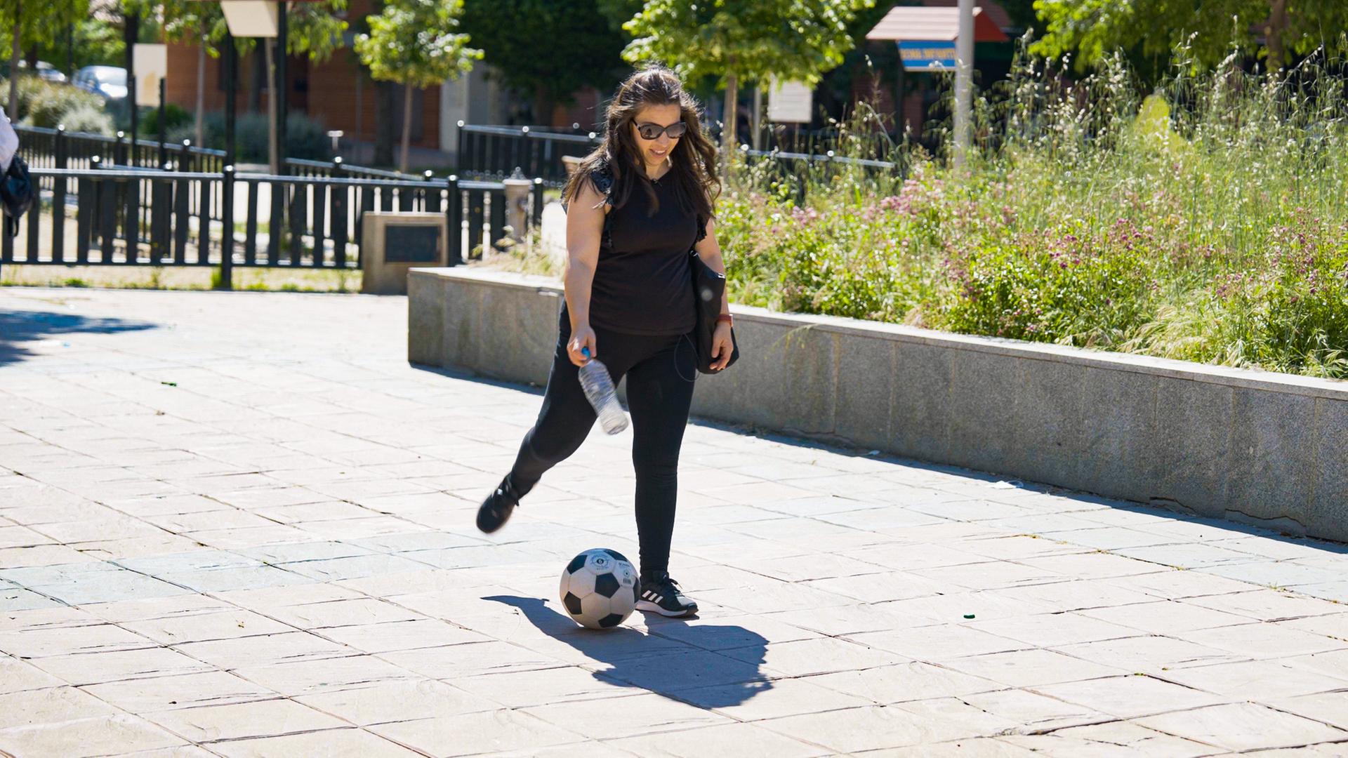 Eine Frau tritt auf der Straße gegen einen Ball.