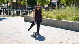 A woman kicks a ball on the street.