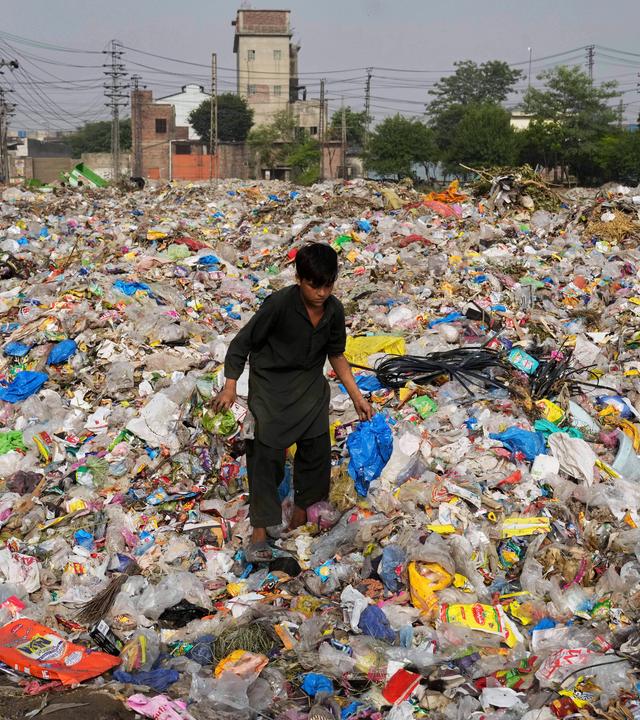 Ein Müllsammler sammelt wiederverwertbare Gegenstände, darunter Plastik, auf einer Mülldeponie.