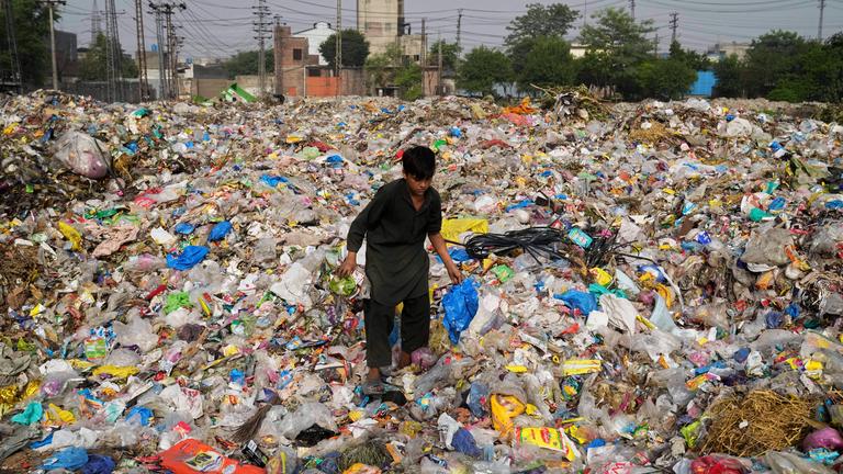 07.08.2025, Pakistan, Lahore: Ein Müllsammler sammelt wiederverwertbare Gegenstände, darunter Plastik, auf einer Mülldeponie.