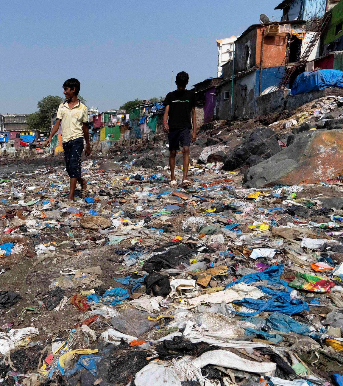 26.11.2024, Indien, Mumbai: Menschen spazieren am Strand des Badhwar Park an der Küste des Arabischen Meeres an Plastikmüll vorbei.