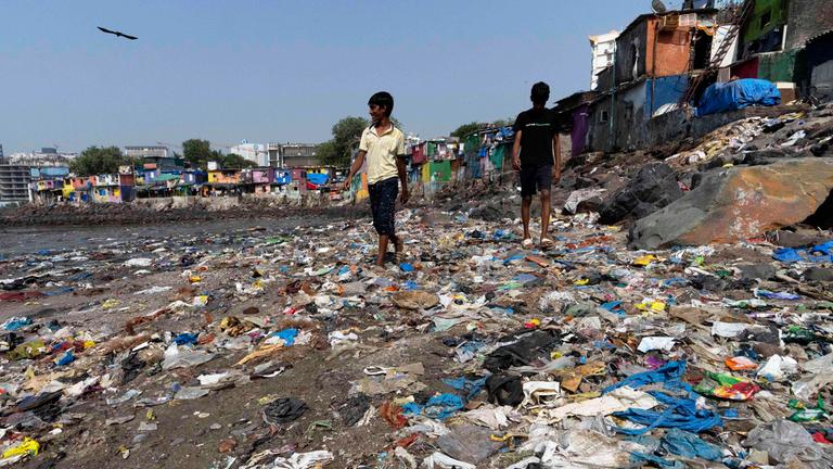 26.11.2024, Indien, Mumbai: Menschen spazieren am Strand des Badhwar Park an der Küste des Arabischen Meeres an Plastikmüll vorbei.