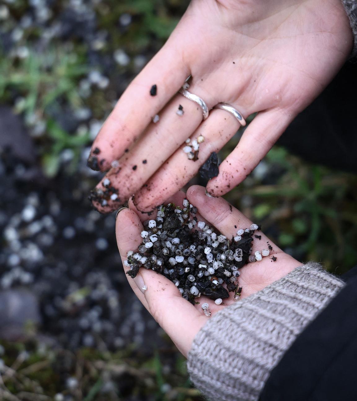 Eine Person sammelt Plastikpellets auf dem Boden in der Nähe eines Industriegebiets.