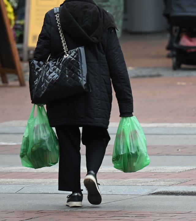 Eine Frau läuft mit zwei vollen Plastiktüten über die Straße. 