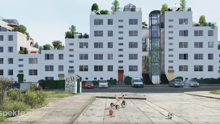 Ein umgebauter Plattenbau der nun aus mehreren Familienhäusern besteht. Die Fassade ist weiß und die Häuser haben viele Fenster. Auf den Dachterassen stehen grüne Pflanzen. Vor dem Haus sind Kinderspielzeuge und Autos.