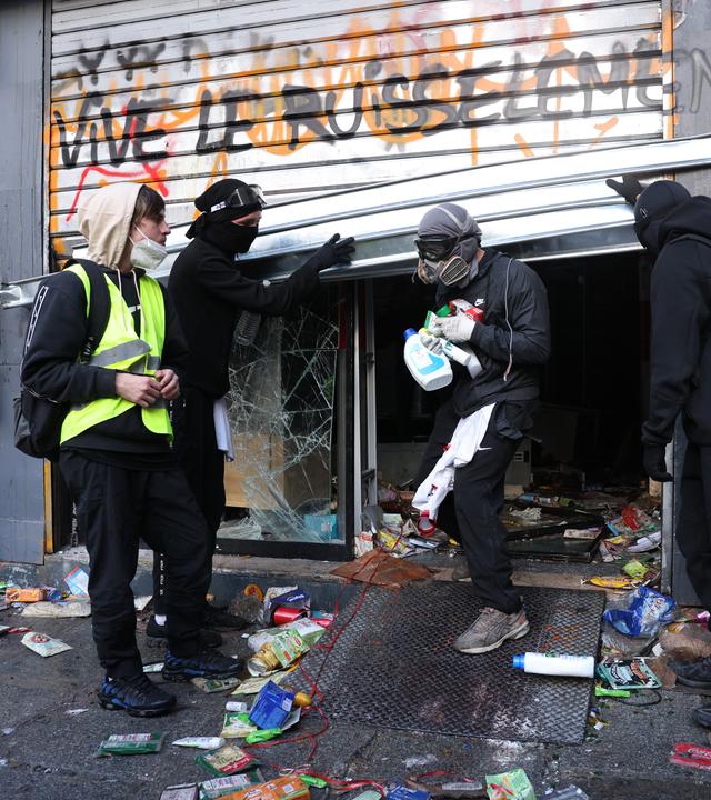 Vermumte Personen steigen aus einem aufgebrochenen Geschäft.