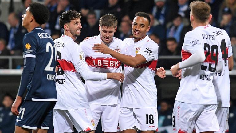 DFB-Pokal: Stuttgarter Spieler jubeln nach einem Treffer zusammen. Ein Bochumer Spieler läuft bedröppelt im Vordergrund vorbei (Unschärfe).