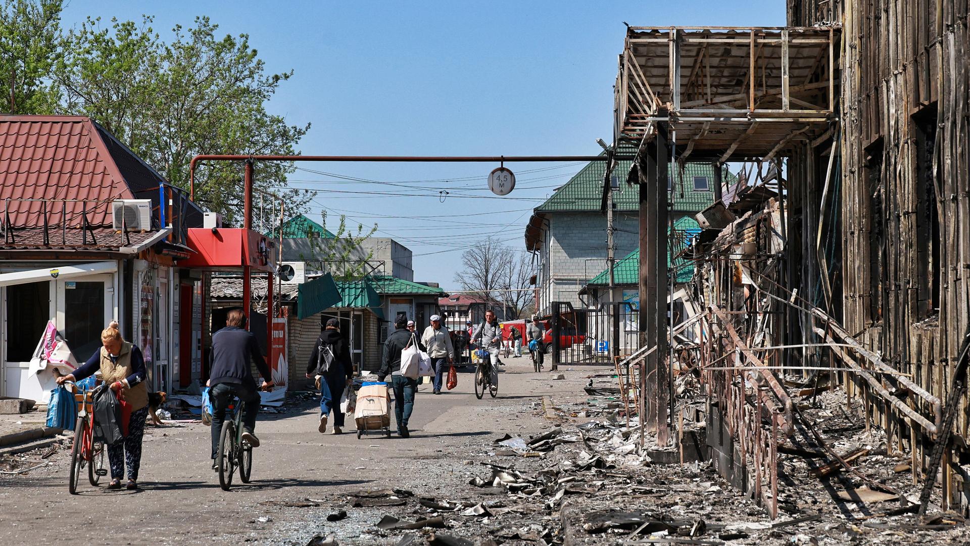 Passanten laufen durch einen zum Teil von russischen Angriffen zerstörten Straßenzug. Aufgenommen im April 2025.