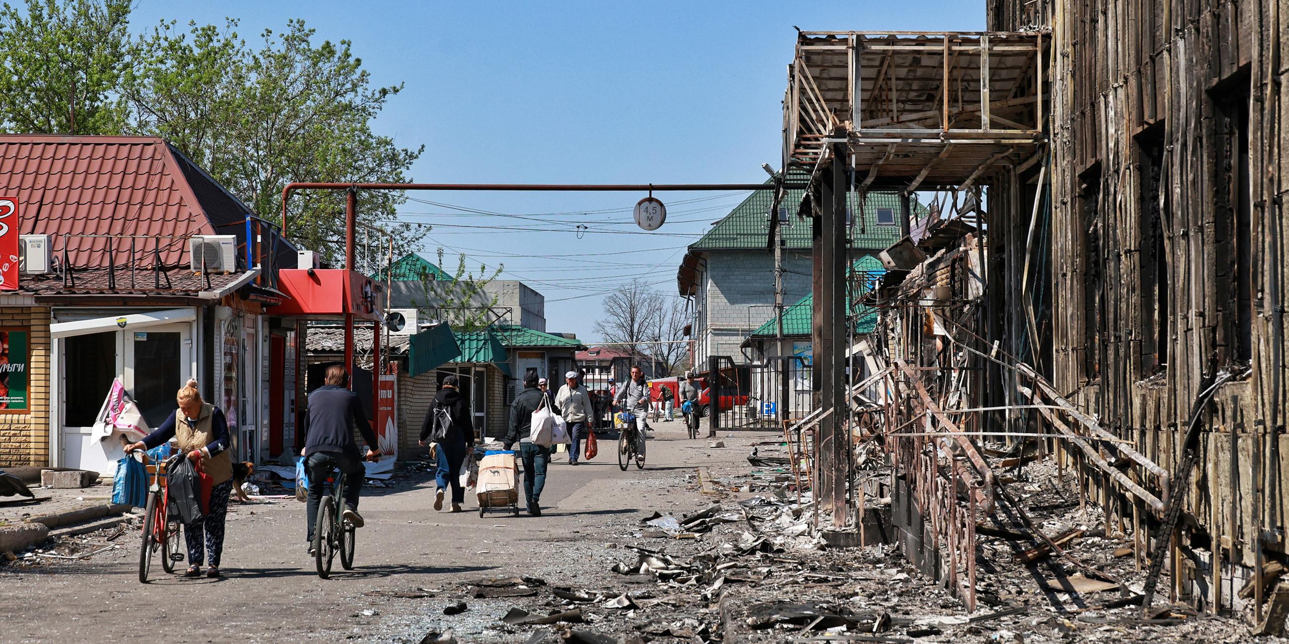 Passanten laufen durch einen zum Teil von russischen Angriffen zerstörten Straßenzug. Aufgenommen im April 2025.