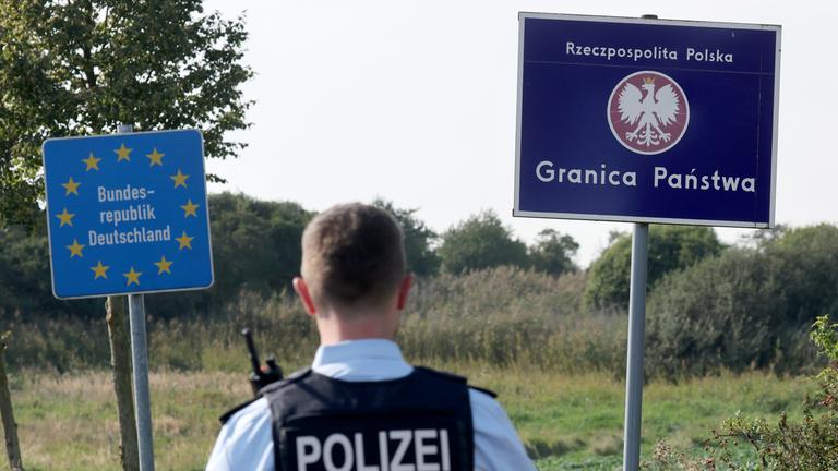 28.09.2023, Mecklenburg-Vorpommern, Linken: Bei einer flexiblen Schwerpunktkontrolle unmittelbar an der deutsch-polnischen Grenze in der Nähe des ehemaligen Grenzübergang Linken steht ein Bundespolizist vor den Schildern für Deutschland und Polen.