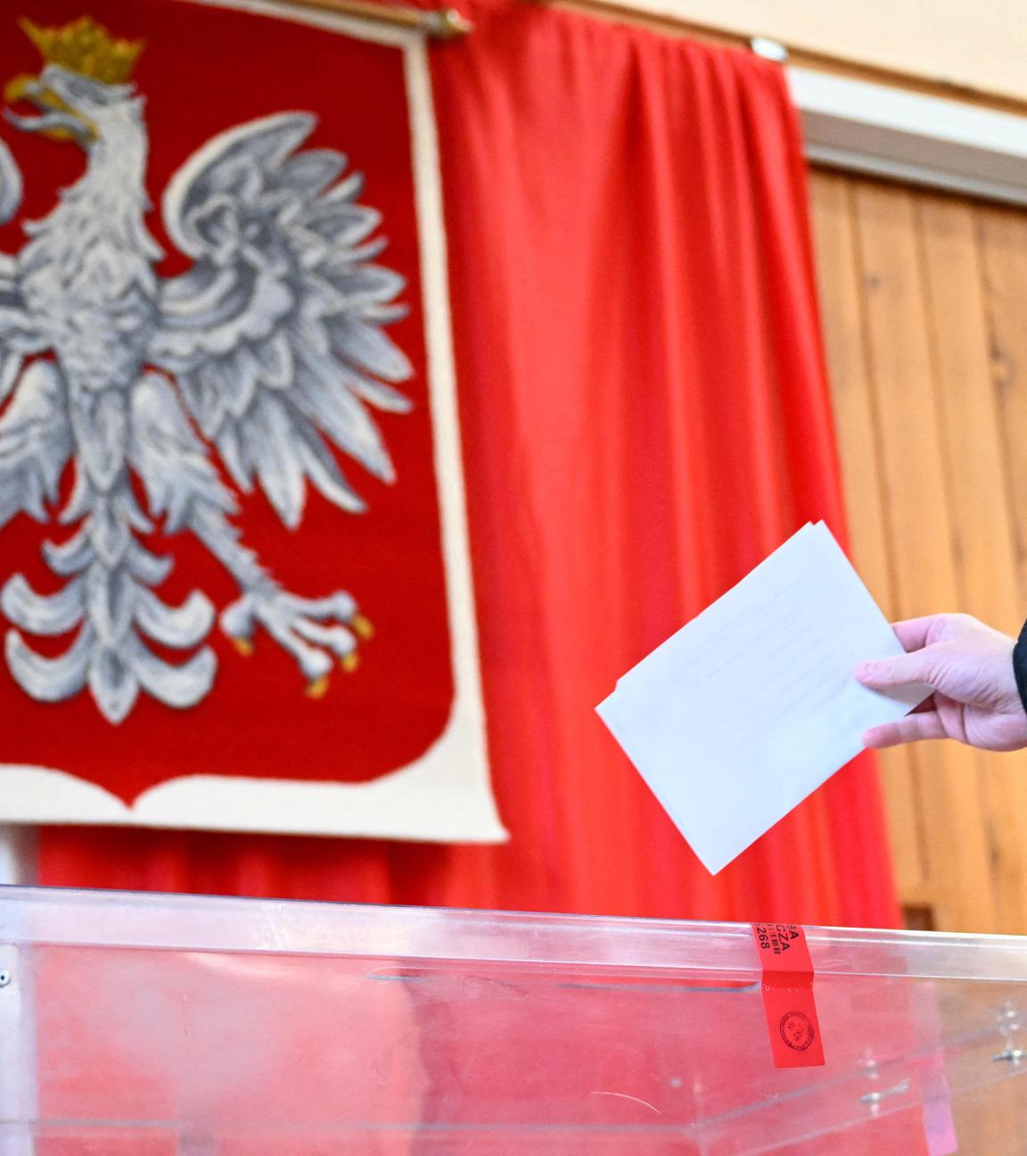Ein Wähler gibt am 18. Mai 2025 in einem Wahllokal in Warschau, Polen, während der ersten Runde der Präsidentschaftswahlen seine Stimme ab, während im Hintergrund das polnische Wappen zu sehen ist.
