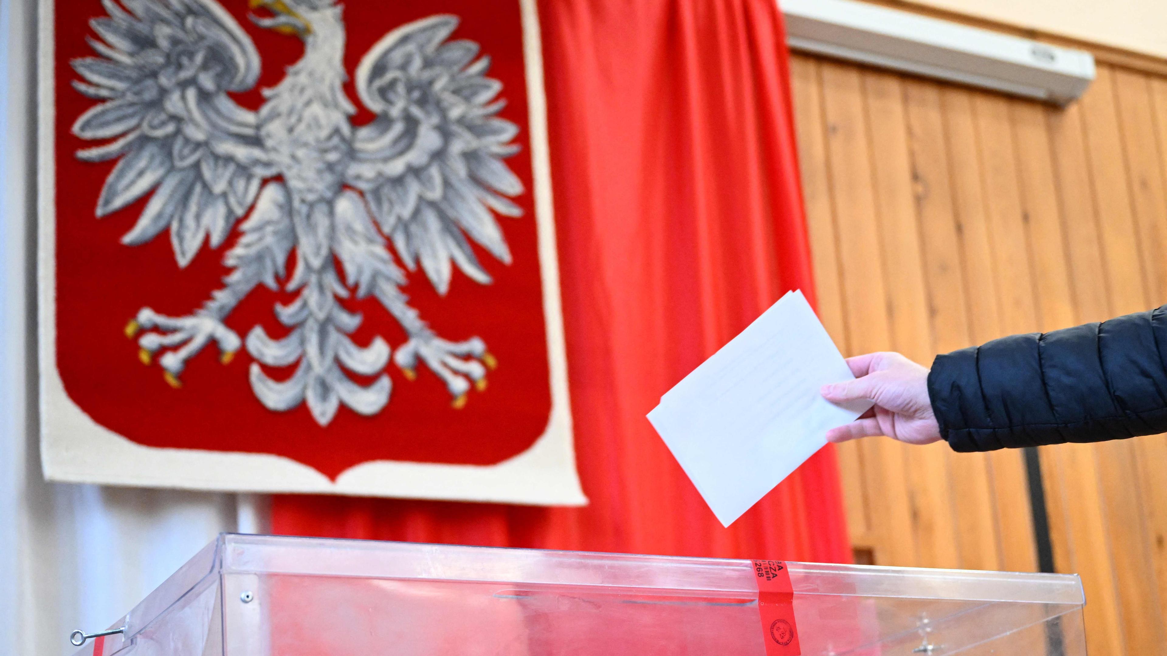 Ein Wähler gibt am 18. Mai 2025 in einem Wahllokal in Warschau, Polen, während der ersten Runde der Präsidentschaftswahlen seine Stimme ab, während im Hintergrund das polnische Wappen zu sehen ist.