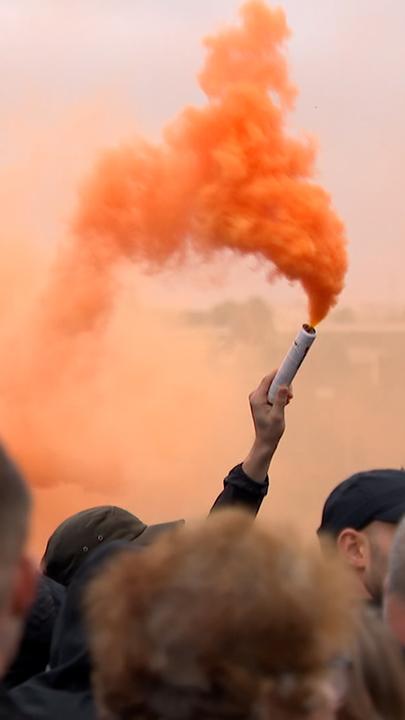 Ein Demonstrant des rechtsextremen Protests in den Niederlanden hält eine Rauchfackel, aus der orangeroter Rauch aufsteigt.
