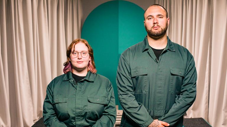 Zwei Menschen in grünen Overalls blicken in die Kamera