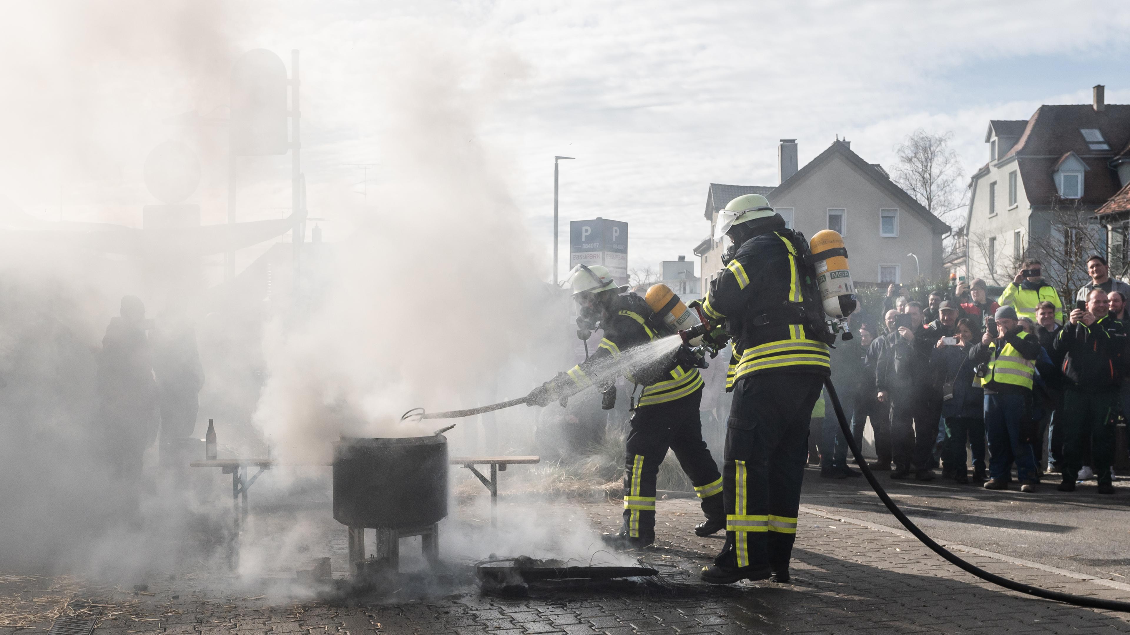 Baden-Württemberg, Biberach an der Riß: Einsatzkräfte der Feuerwehr löschen ein Feuer, das Demonstranten beim politischen Aschermittwoch der baden-württembergischen Grünen vor der Stadthalle von Biberach an der Riß angezündet haben.