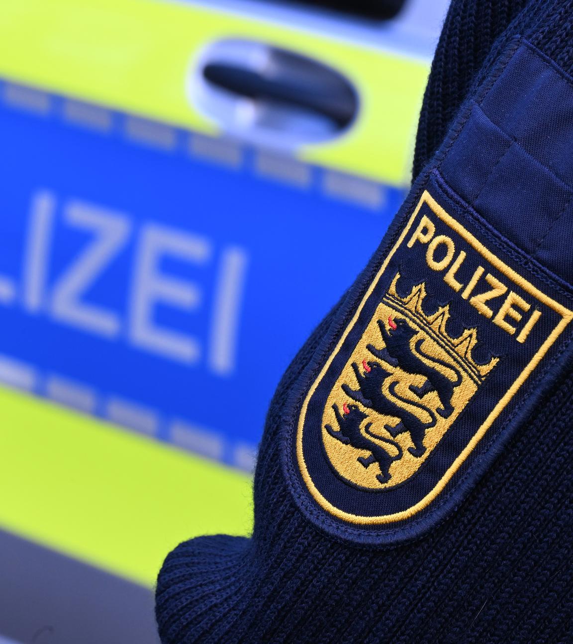 Wappen der Polizei auf Uniform eines Polizisten vor seinem Polizeiwagen.