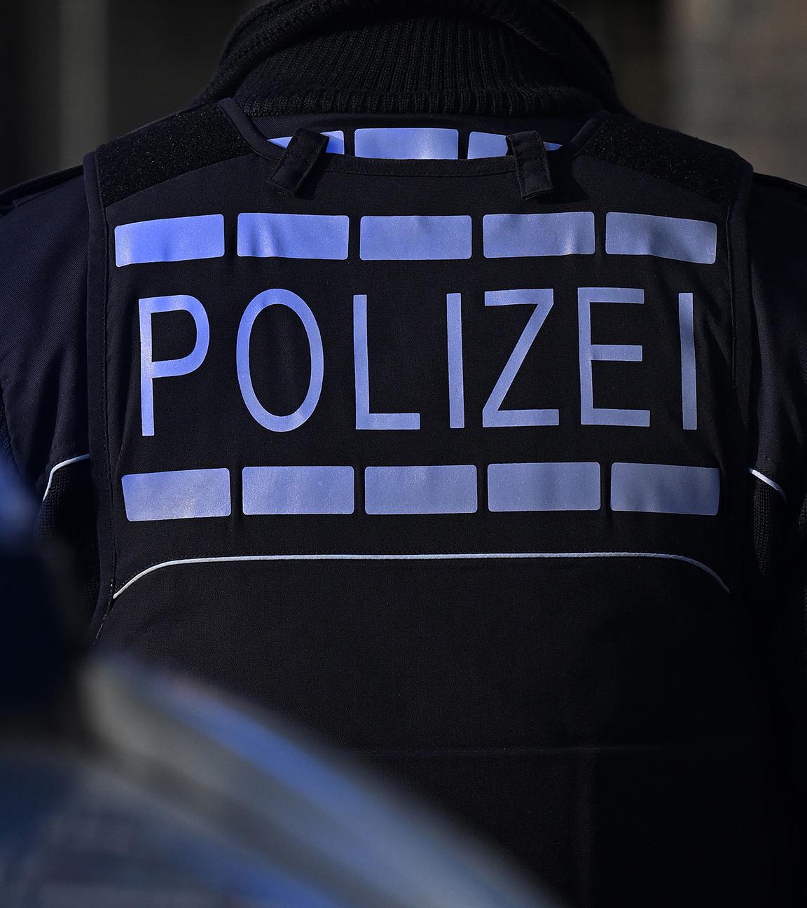 Das Logo der Polizei auf der Dienstkleidung von Polizisten die vor einem Blaulicht stehen
