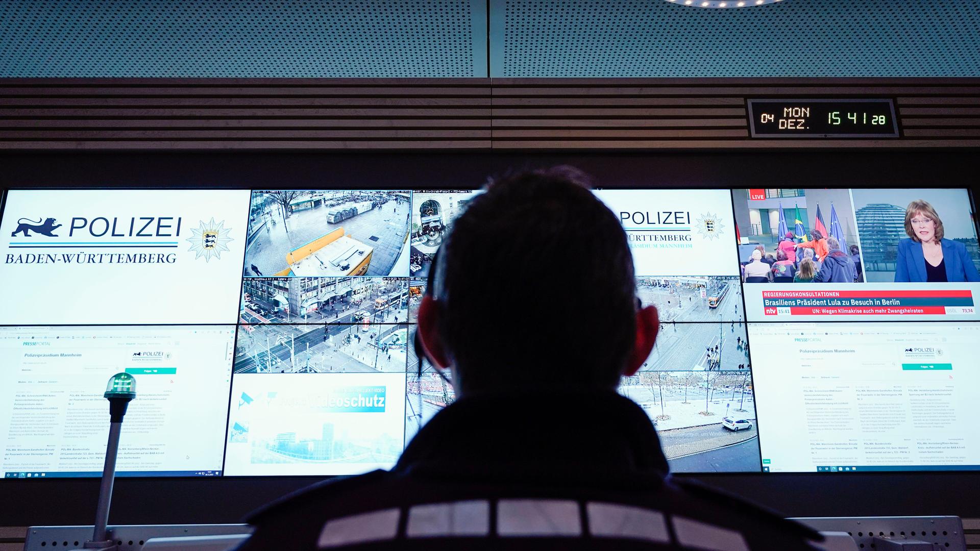 Archiv:  Ein Beamter steht im Führungs- und Lagezentrum des Polizeipräsidiums Mannheim vor einer Wand mit Bildschirmen. 