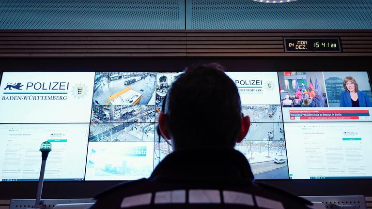 Archiv:  Ein Beamter steht im Führungs- und Lagezentrum des Polizeipräsidiums Mannheim vor einer Wand mit Bildschirmen. 