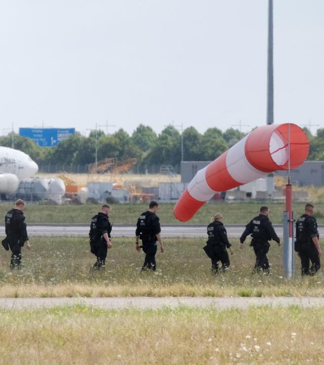 Polizisten gehen über eine Wiese auf dem Gelände des Flughafen-Leipzig am 07.08.2026.