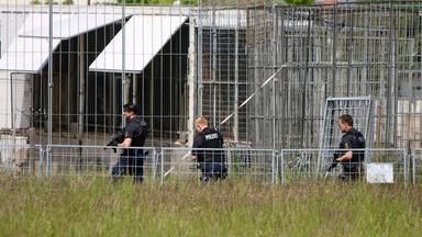 Bewaffnete Polizeibeamte laufen an Käfigen vorbei.