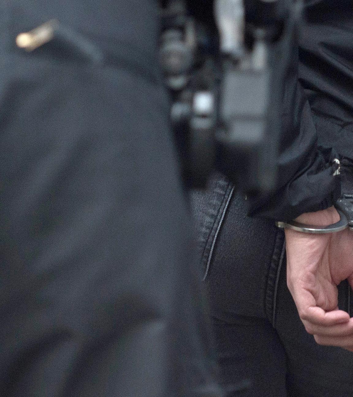Ein Polizist hältt einen Mann in Handschellen fest (Archivfoto)