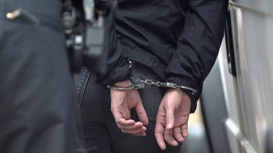 Ein Polizist hältt einen Mann in Handschellen fest (Archivfoto)
