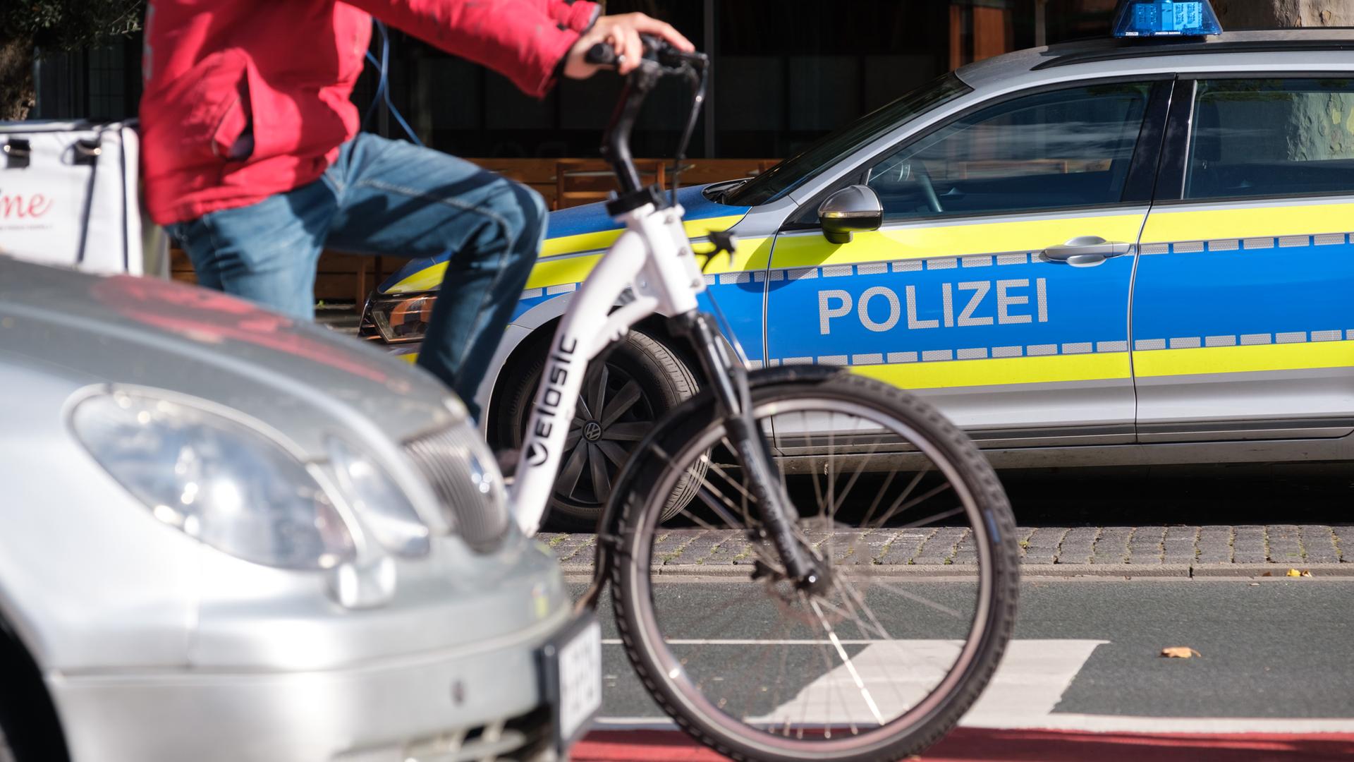 Niedersachsen, Hannover: Ein Polizeiauto steht neben einer viel befahrenen Straße, auf der neben einem Auto ein Fahrradfahrer auf einem Radweg hält.