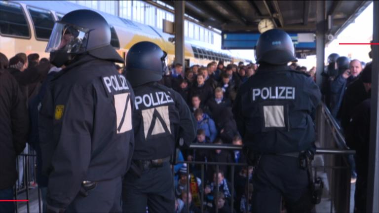 Polizisten auf einem Bahnsteig beobachten anreisende Fußballfans 