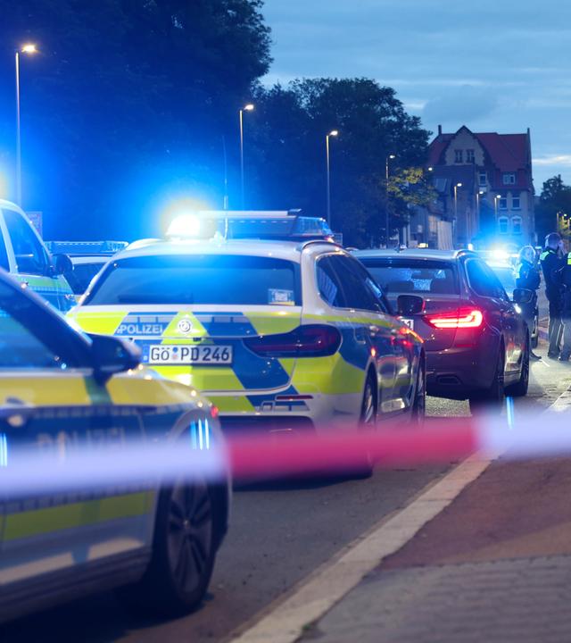 Polizisten und Polizeifahrzeuge stehen in Göttingen hinter einer Absperrung.