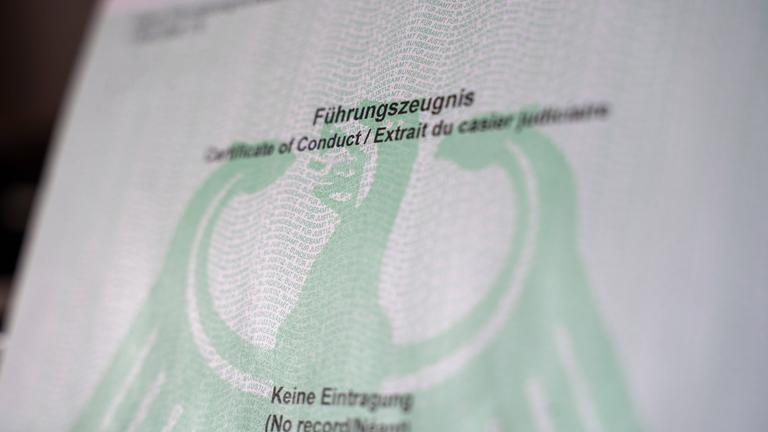 Auf einem Dokument steht "Führungszeugnis" und "keine Eintragung", jeweils mit englischer und französischer Übersetzung. Dahinter ist in grün der Bundesadler abgebildet.