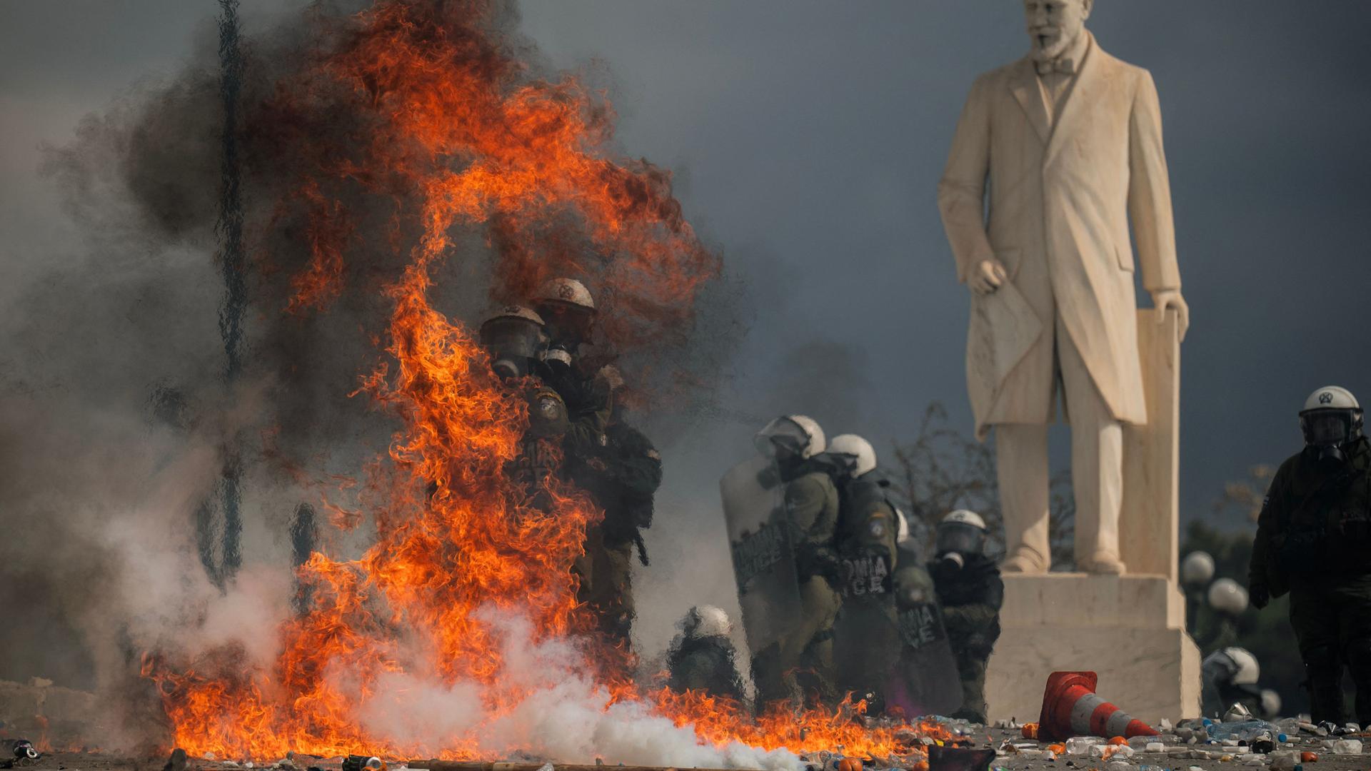 Polizisten stehen neben der Statue von Eleftherios Venizelos und suchen Schutz vor Molotowcocktails