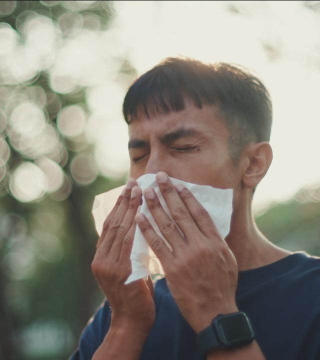 Mann niest in ein Taschentuch.