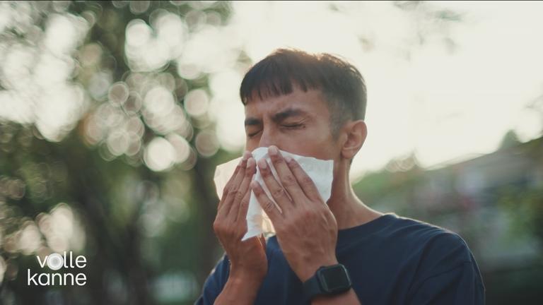 Mann niest in ein Taschentuch.