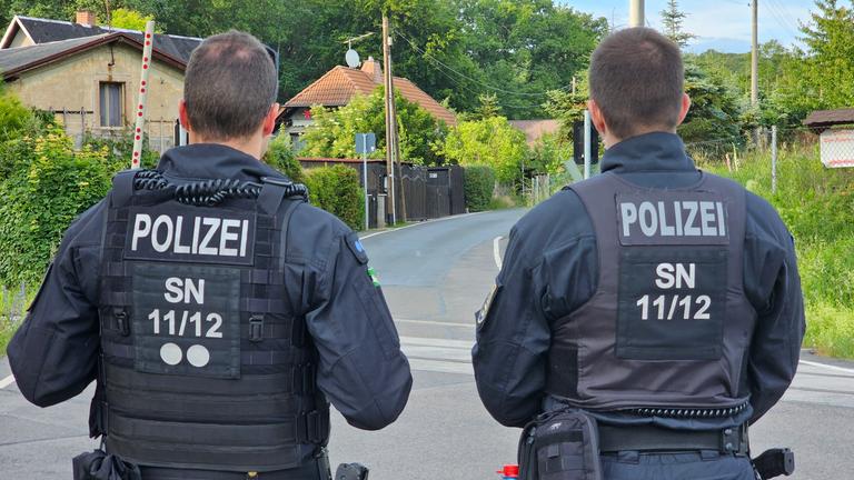 Sachsen, Mahlitzsch: Zwei Polzisten stehen auf einer Straße.