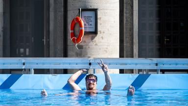 Norman, Mitarbeiter der Volksbühne, treibt im temporären Schwimmbad, das vor der dem Berliner Theater aufgebaut wird, am 30.07.2026.