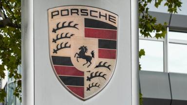 Das Porsche aussen am Gebaeude, Das Porsche-Logo ist ein goldfarbenes Wappen mit rotem und schwarzem Streifenmuster, Hirschgeweihen, einem springenden schwarzen Pferd und der Aufschrift Stuttgart, gekroent vom Schriftzug Porsche.