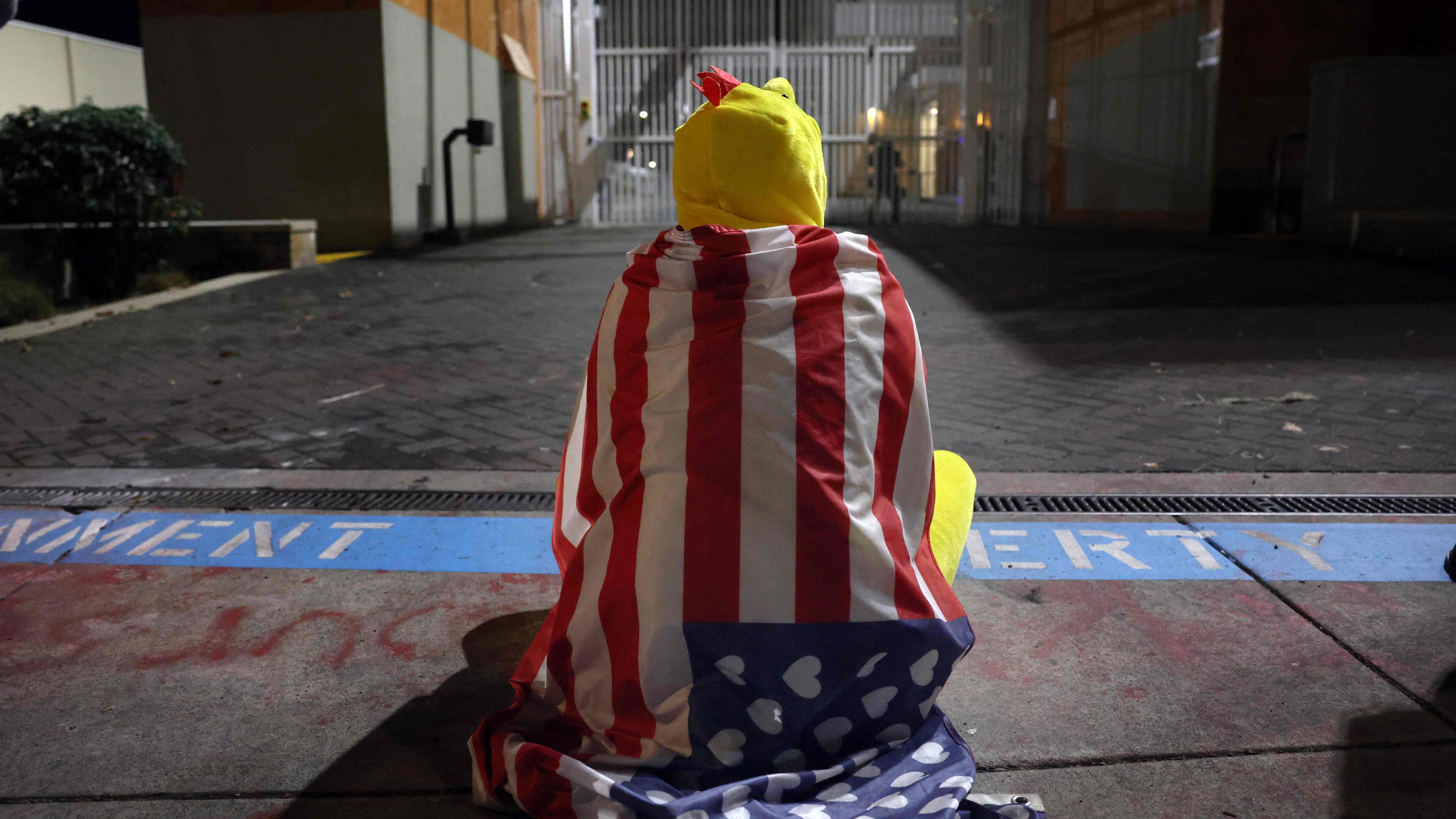 Ein Mann in einem Hühnerkostum sitzt vor einem Gebäude der US-Einwanderungsbehörde in Portland.