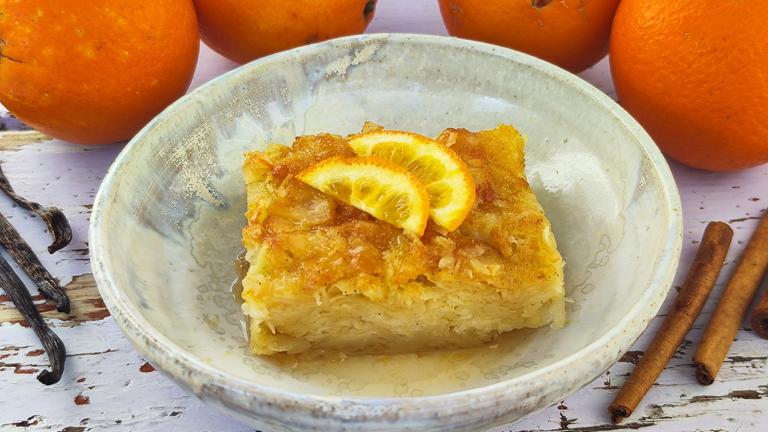 Tiefer Teller mit dem griechischen Orangenkuchen "Portokalópita", getoppt mit zwei Stücken einer Orange.