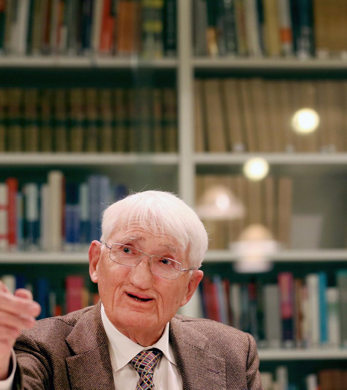 Jürgen Habermas sitzt vor einem Bücherregal und zeigt mit dem Finger an der Kamera vorbei.